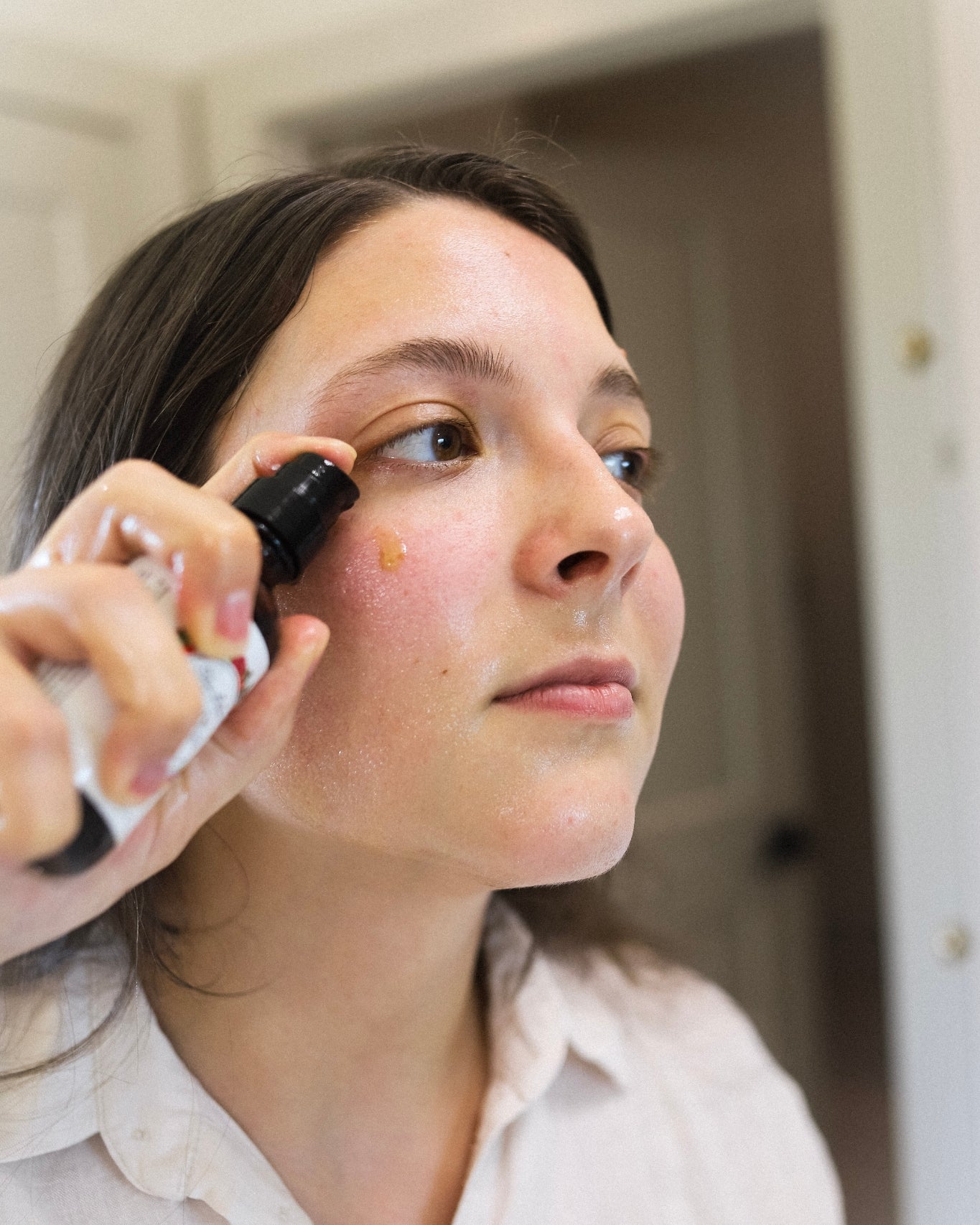 A close-up shot of a woman squirting the Renew Cleansing Oil onto her cheek.