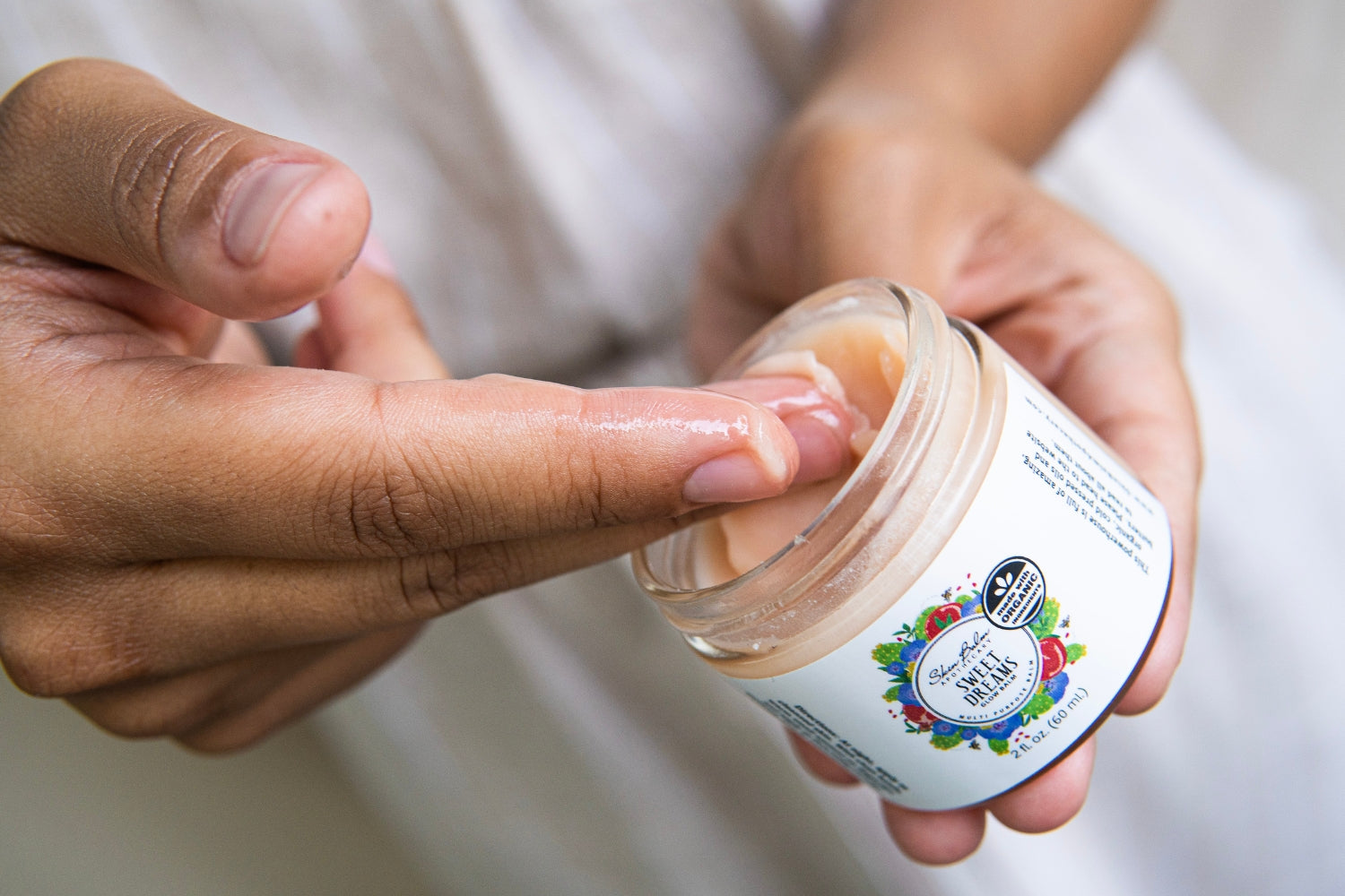 A close-up shot of a woman scooping the Sweet Dreams Glow Balm out of the jar with her fingers.